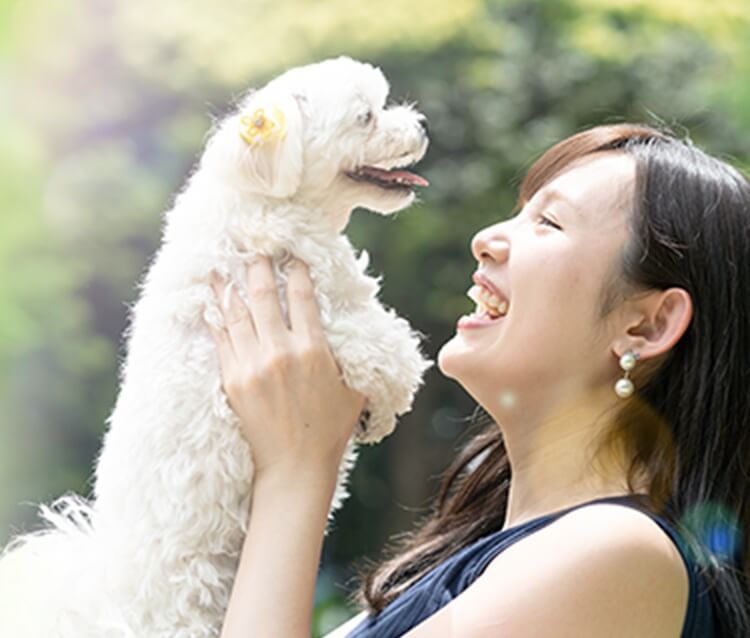 女性がワンちゃんを抱きかかえて笑っている