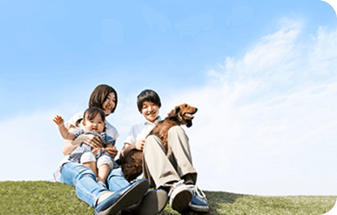 ワンちゃんを抱っこしている男性と子どもを抱っこしている女性が土手のような場所に座っている