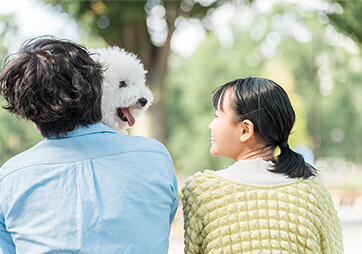 ワンちゃんを抱っこしている男性と女性が並んで、こちらに背中を向けている
