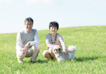 男性と女性がしゃがんでいて、女性の前にはワンちゃんが立っている